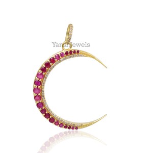 May include: Gold crescent moon pendant with a row of pink and white gemstones. The pendant is on a white background. Yans Jewels.