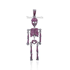 May include: A silver skeleton pendant featuring a skull head and pink gemstones. The pendant is detailed with a heart-shaped design on the chest and is a unique piece of jewellery.