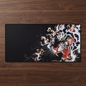 May include: A rectangular desk mat featuring a black background on the left side and a detailed illustration of a roaring tiger on the right. The tiger is depicted with white fur, black stripes, and red accents, surrounded by swirling smoke-like patterns.