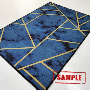 Puede incluir: Alfombra geom&eacute;trica azul y dorada con efecto m&aacute;rmol. La alfombra tiene un borde negro.