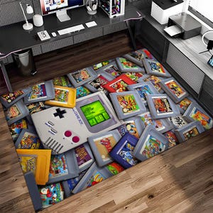 Könnte beinhalten: Ein bunter Teppich mit einem Vintage Game Boy und verschiedenen Retro-Videospielkassetten. Der Teppich ist aus einem weichen, strapazierfähigen Material gefertigt und perfekt, um jedem Raum einen Hauch von Nostalgie zu verleihen.