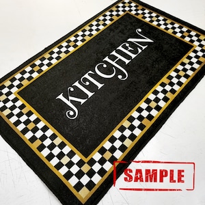 Puede incluir: Alfombra de cocina a cuadros en blanco y negro con borde dorado. La alfombra tiene la palabra "KITCHEN" impresa en blanco sobre fondo negro.