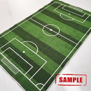 Puede incluir: Alfombra de campo de f&uacute;tbol verde y blanco con l&iacute;neas blancas y un c&iacute;rculo central. La alfombra tiene un borde blanco y la palabra "SAMPLE" est&aacute; impresa en rojo sobre un fondo blanco.