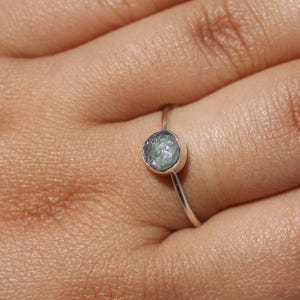 Könnte beinhalten: Ein silberner Ring mit einem runden, grauen Edelstein. Der Ring befindet sich an einem Finger.