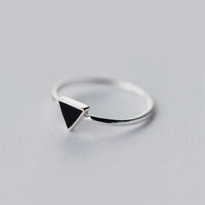 May include: A minimalist silver ring featuring a black triangle design. The ring has a thin band and a geometric shape, perfect for everyday wear. The ring is a simple yet stylish accessory.