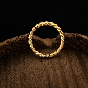 Puede incluir: Un anillo dorado que presenta un diseño de cuerda trenzada continua. La banda está elaborada con un acabado metálico pulido, creando un patrón de espiral uniforme a lo largo de toda la circunferencia de la pieza de joyería circular.