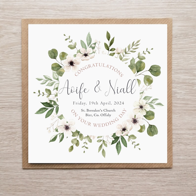 May include: A square wedding card featuring a watercolour floral wreath of white flowers and green leaves surrounding the text: CONGRATULATIONS, Aoife & Niall, Friday, 19th April, 2024, St. Brendan's Church, Birr, Co. Offaly, ON YOUR WEDDING DAY.