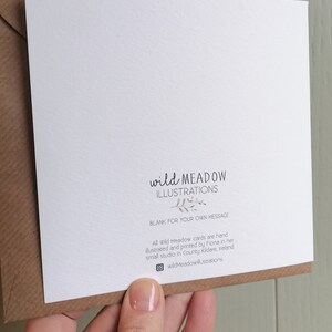 May include: A square white greeting card with a brown envelope. The card features the text "wild MEADOW ILLUSTRATIONS" with a small leaf graphic, "BLANK FOR YOUR OWN MESSAGE", and additional text detailing the hand-illustrated production in Ireland.
