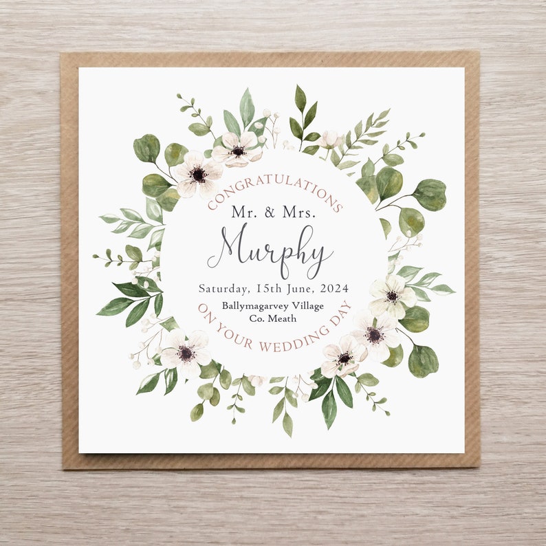 May include: A square wedding greeting card featuring a watercolour floral wreath of white anemone flowers and green eucalyptus leaves. The centre text reads: CONGRATULATIONS Mr. & Mrs. Murphy Saturday, 15th June, 2024 Ballymagarvey Village Co. Meath ON YOUR WEDDING DAY.