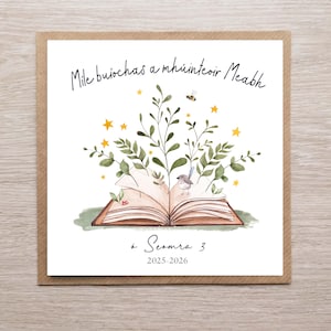 May include: A square greeting card featuring a watercolour illustration of an open book with foliage, a bird, and a bee. The card has text in Irish, with the words "Mile buíochas a mhúinteoir Meabh" and "á Seomra 3 2025-2026". The card is on a brown background.