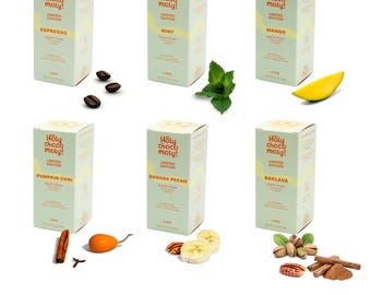 May include: Six boxes of gourmet hot chocolate mix with different flavors: Espresso, Mint, Mango, Pumpkin Chai, Banana Pecan, and Baklava. Each box features a green and white design with the brand name "Holy Choco Moly!" and the flavor name.