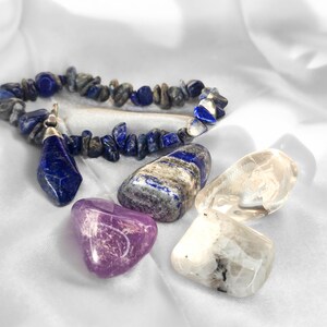 May include: A lapis lazuli chip bracelet with a faceted pendant, accompanied by a polished lapis lazuli stone, a translucent purple amethyst, a clear quartz crystal, and a smooth white moonstone with dark inclusions.