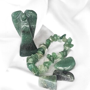 May include: A collection of green aventurine crystals and a carved angel figurine. The assortment includes a bracelet made of small, irregular stones, and several polished, larger stones. The angel is carved with detailed wings.