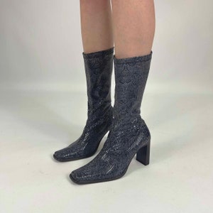 Può includere: Un paio di stivali neri in pelle di serpente con tacco a blocco e punta a punta.