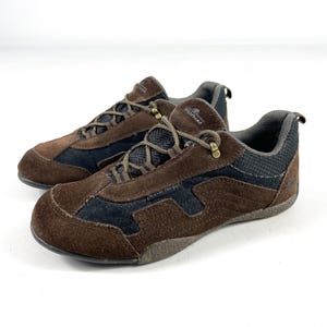 May include: A pair of brown and black suede and mesh athletic shoes. The shoes have brown laces, a padded collar, and a rubber sole. The brand name "SportHead" is visible on the side of the shoe. The shoes are waterproof.