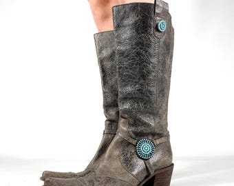May include: A pair of distressed grey leather knee-high boots. The boots have a pointed toe, a small heel, and turquoise-coloured embellishments. The leather has a textured, crackled appearance.