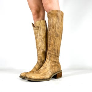 May include: Knee-high boots with a snakeskin design. The boots are light brown and have a textured finish. They feature a small heel and a side zip. The boots are made from a leather-like material, suitable for various outfits.
