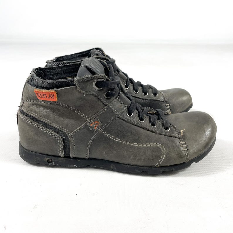 May include: A pair of gray leather ankle boots with black laces and soles. The boots have a distressed look, with visible stitching and the brand name "REPLAY" on a small orange tag.
