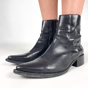 以下が含まれることがあります： 黒革のポインテッドトゥのアンクルブーツで、低いブロックヒールが付いている