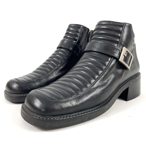 May include: Pair of black leather ankle boots with a quilted design. The boots have a square toe, a chunky heel, and a buckle closure on the side. The boots are on a white background.