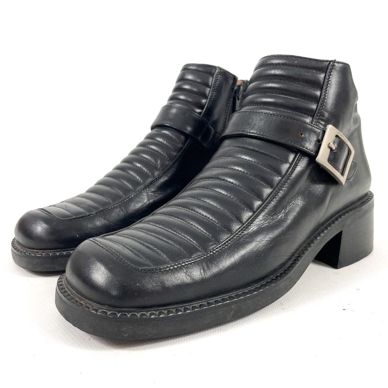 May include: Pair of black leather ankle boots with a quilted design. The boots have a square toe, a chunky heel, and a buckle closure on the side. The boots are on a white background.