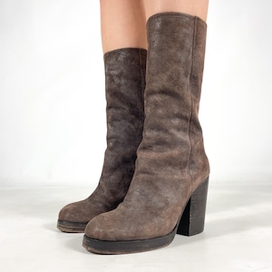 May include: Brown suede knee-high boots with a block heel and platform sole. The boots have a textured appearance and a rounded toe. The heel is approximately 4 inches high.