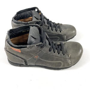 May include: A pair of gray leather ankle boots with black laces. The boots have a distressed look with visible stitching and a small orange accent. The interior of the boots is visible, and the soles are dark.