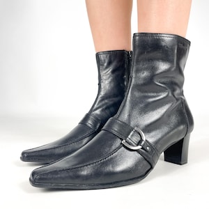 Peut inclure: Bottines en cuir noir à bout pointu et boucle argentée. Les bottes ont un talon bloc bas.