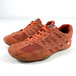 Könnte beinhalten: Paar orangefarbene Wildleder- und Mesh-Sneaker mit orangefarbenen Schnürsenkeln. Die Sneaker tragen den Markennamen "GEOX" auf der Seite und eine braune Sohle. Die Schuhe sind für sportliche Aktivitäten konzipiert.