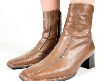 May include: Brown leather ankle boots with a square toe and a low block heel. The boots have a zipper on the inside of the ankle and decorative stitching on the front.