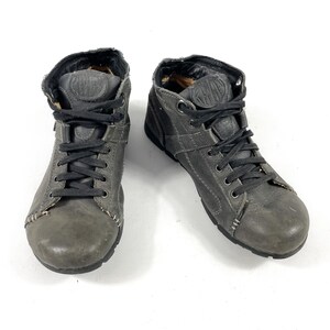 May include: A pair of gray leather high-top sneakers with black laces. The shoes have a worn appearance and feature stitching details and a logo on the tongue. The sneakers are designed for casual wear.