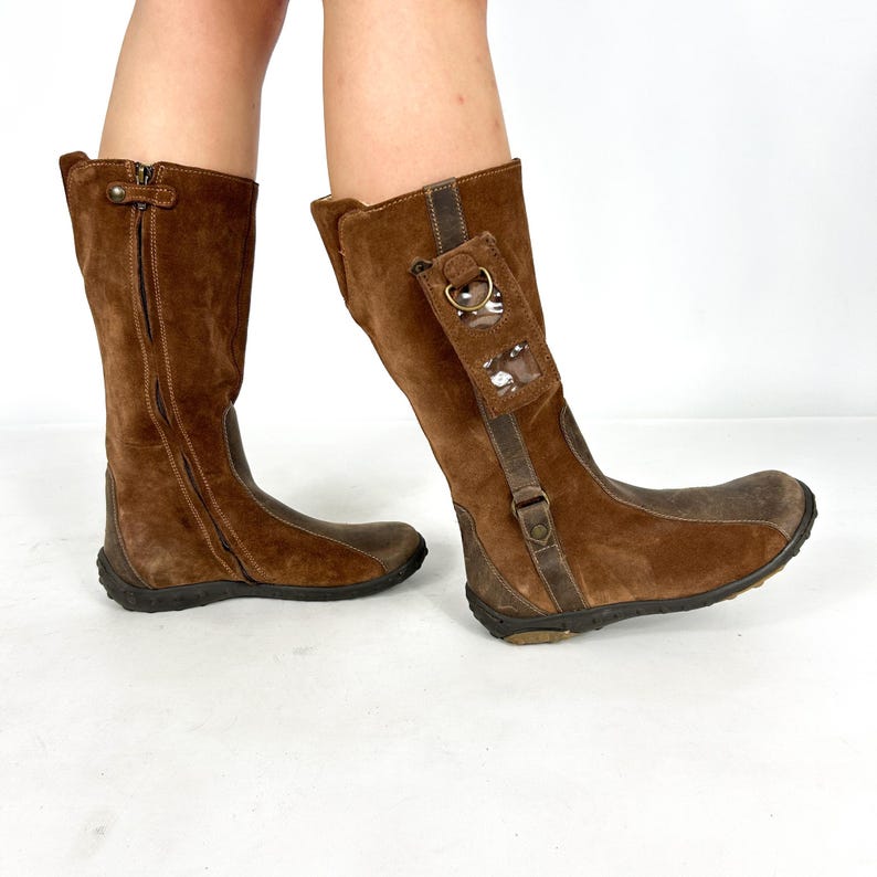 May include: Brown suede knee-high boots with a zipper on the side and a clear plastic pocket on one boot.