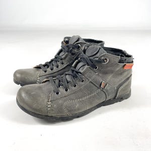 May include: A pair of gray leather ankle boots with black laces. The boots have a rugged, worn appearance with visible stitching and a textured finish. The soles are black, and the boots appear to be well-constructed.
