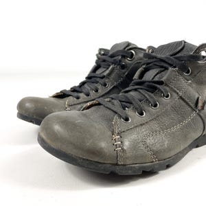May include: A pair of gray leather boots with black laces. The boots have a worn appearance, with visible stitching and a textured surface. The soles are black, and the boots appear to be ankle-high.