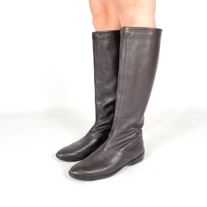 Puede incluir: Un par de botas de cuero marrón de caña alta con suela plana.