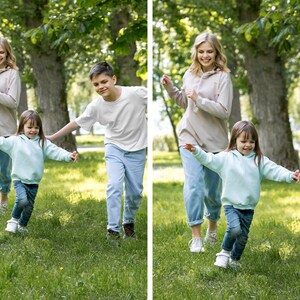 May include: Three people, two adults and a child, are running and laughing in a grassy park. The adults are wearing casual clothing, while the child is wearing a light blue hoodie. The adults are both female and have long, straight hair. The child is female and has short, curly hair.