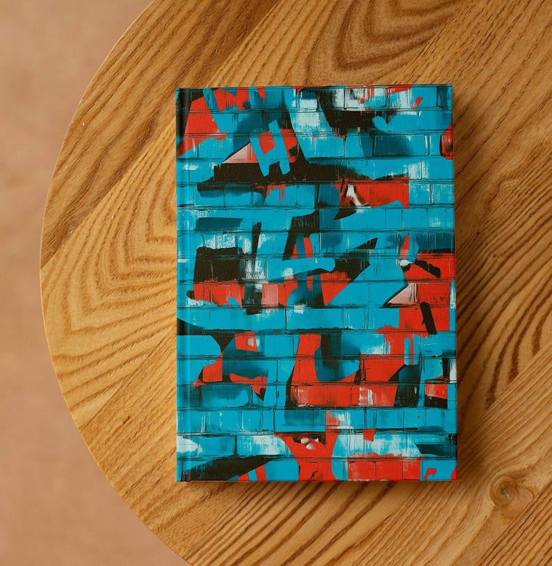 Op de afbeelding: Een rechthoekig notitieboek met een levendig graffiti-achtig ontwerp. De omslag heeft een baksteenpatroon in tinten blauw, rood en zwart. Het notitieboek ligt op een houten oppervlak.