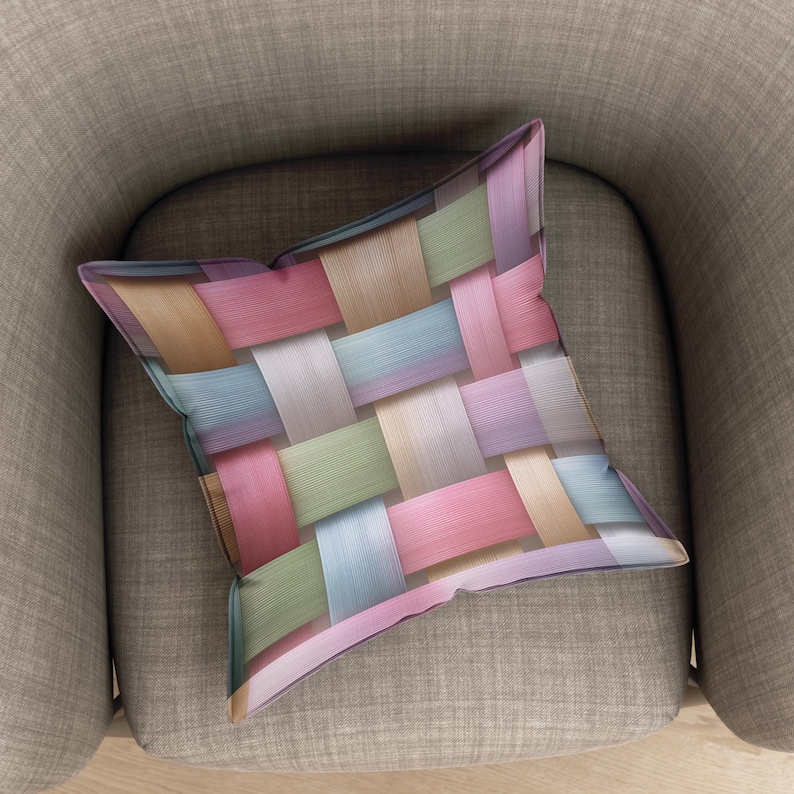 May include: A decorative square pillow with a woven pattern in pastel colors, including pink, blue, green, and beige. The pillow is resting on a gray armchair, showcasing its design and texture. The pillow's design is reminiscent of a basket weave.