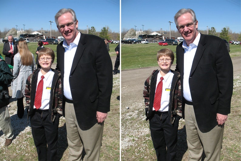May include: Two men and a boy are standing together. The man on the left is wearing a black suit and a white shirt. The man on the right is wearing a black suit and a white shirt. The boy is wearing a black jacket, a white shirt, a red tie, and blue pants.