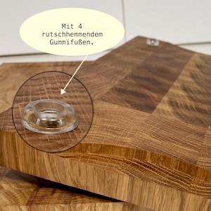 May include: Close-up of a wooden cutting board with a clear, rubber foot. The board has a natural wood grain pattern and is light brown. The text in the image says "With 4 non-slip rubber feet."