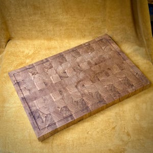 May include: A rectangular end-grain butcher block cutting board. The board is made of light and dark brown wood pieces arranged in a mosaic pattern. A juice groove runs around the perimeter of the board.