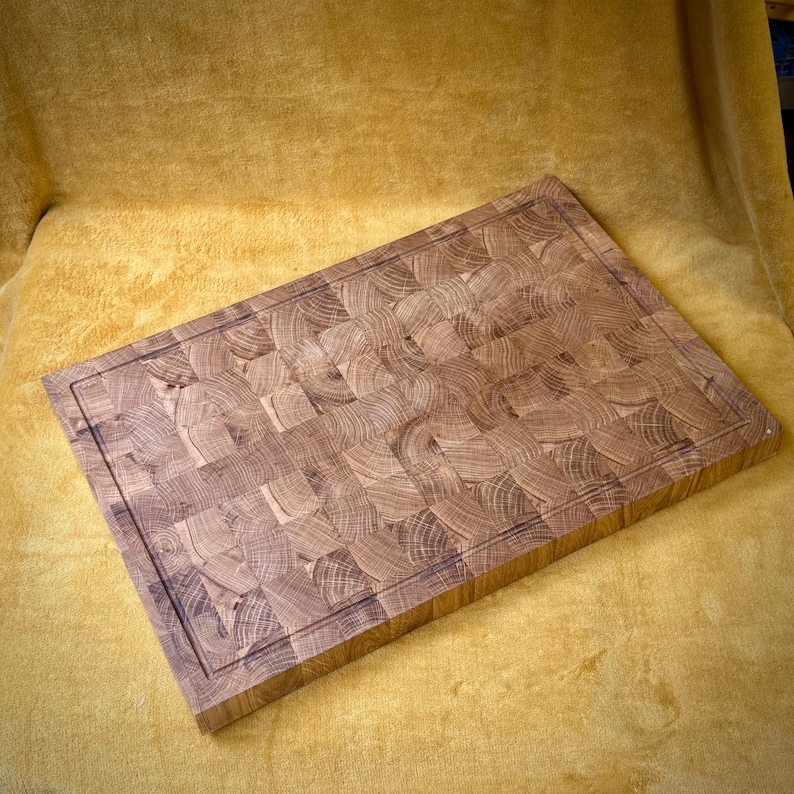 May include: A rectangular end-grain butcher block cutting board. The board is made of light and dark brown wood pieces arranged in a mosaic pattern. A juice groove runs around the perimeter of the board.
