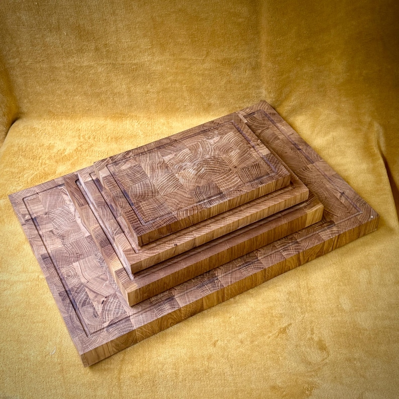 May include: A stack of four wooden cutting boards of varying sizes. The boards are made of light brown wood with a block pattern and a dark border. The boards are arranged from largest to smallest, creating a layered effect.