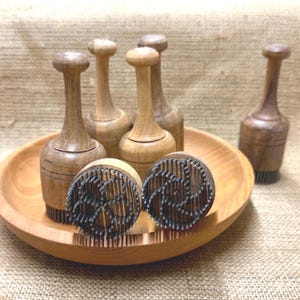 Op de afbeelding: Een verzameling vintage houten botermallen en -stempels. De mallen hebben een afgeronde bovenkant en een cilindrisch lichaam. De stempels hebben een cirkelvormig ontwerp met metalen pinnen. De items worden gepresenteerd op een houten bord.