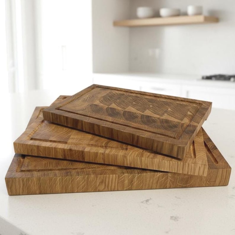 May include: Three wooden cutting boards of varying sizes are stacked on top of each other. The boards are rectangular with a juice groove around the edges. The wood grain is visible, and the boards have a natural, warm brown color.