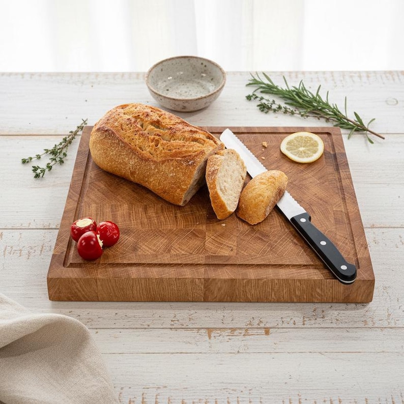 May include: A wooden cutting board with a loaf of sliced bread, a bread knife, and a small bowl. The bread is golden brown, and the knife has a black handle. Red peppers and a lemon slice are also on the board.