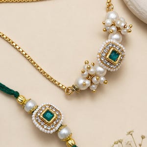 May include: A gold-toned box chain necklace featuring a central square emerald-green stone surrounded by clear crystals and clusters of white pearls. Below it, a green thread bracelet features a matching square emerald-green stone.