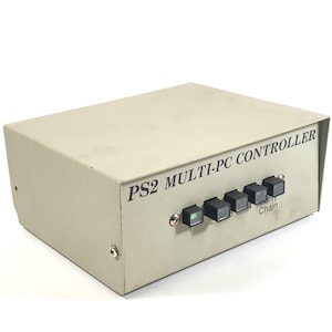 May include: A beige PS2 Multi-PC Controller with black buttons and the word "Chain" printed on the front. The device has a rectangular shape and is made of metal.