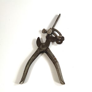 Könnte beinhalten: Ein antikes, rostiges Metallwerkzeug mit gebogenen Griffen und einem komplexen Mechanismus. Das Werkzeug hat zangenartige Backen und verstellbare Teile. Das Design deutet darauf hin, dass es für eine spezielle Aufgabe verwendet wurde.