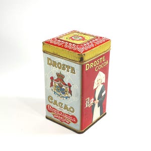 May include: Vintage Droste Cocoa tin with a red, yellow, and blue color scheme. The tin features the words "DROSTE COCOA" and "CACAO" with a royal crest and an image of a woman in a white bonnet.